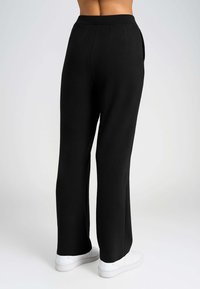 Pantaloni neri a gamba larga realizzati in tessuto leggero, caratterizzati da una texture liscia, un design plissettato, tasche laterali e una vita alta.