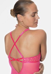 Rosa simdräkt med nät-bakdel och korsade axelremmar samt metalliska detaljer. Slät tyg med en livlig nyans och konturerad form.