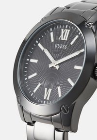 Schwarze Edelstahl-Uhr mit einem strukturierten Zifferblatt und silbernen Stundenmarkierungen. Enthält eine Datumsanzeige und ein Gliederarmband.