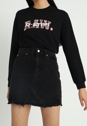 Kobieta w czarnej koszulce z długim rękawem z wzorzystym napisem "G-STAR" oraz czarnej, wysokowarstwowej, postrzępionej mini spódnicy z denimu.