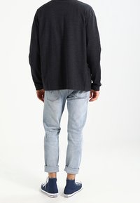 Ciemnoszara koszula z długim rękawem, jasnoniebieskie jeansy z podwiniętymi nogawkami oraz niebieskie trampki typu high-top; prosty fason z podwiniętymi rękawami i subtelną fakturą.