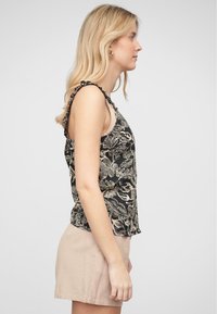 Top in stile canotta nera con motivo floreale, spalline volant e vestibilità rilassata. Abbinato a pantaloni corti beige chiaro. Tessuto morbido e leggero.