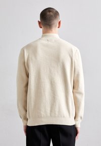 Beiger, strukturierter Strickpullover mit Kragen und gerippten Bündchen. Hat einen geraden Saum. Der Stoff wirkt weich und gemütlich.