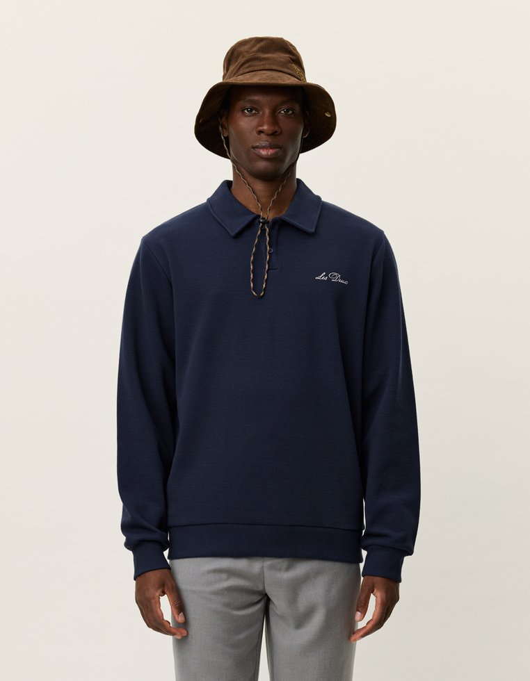 Jūras zila garām piedurknēm polo krekls ar apkakli, ar logo uz krūtīm un ribotām piedurknēm. Kombinēts ar brūnu kausa formā cepuri.