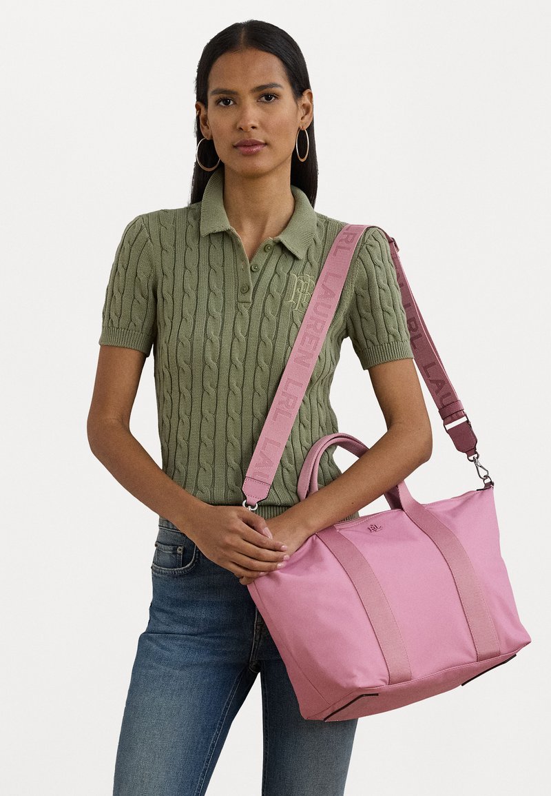 Rosa totebag med to topphåndtak og en avtakbar stropp. Har myk stoff, kontrastfargede stropper og en logo på forsiden.
