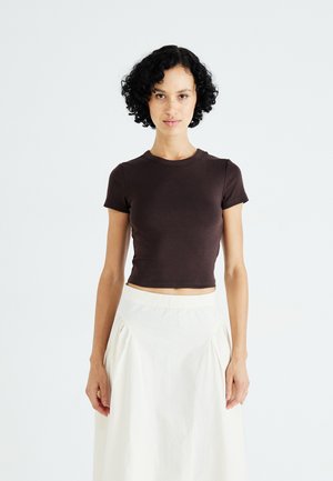 Brun cropped t-shirt med korte ærmer, lavet af blødt stof. Sammen med en hvid, flydende nederdel med subtile plisseringer og elastisk talje.