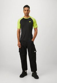 Lühikeste varrukatega must ja neoonrohelise tooniga sportlik särk, mida on kombineeritud mustade kergelt laienevate pükstega, millel on mitu taskut, ning mustade tennistega.