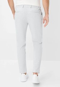 Light gray jogger pants made of cotton blend, tapered fit, with two back pockets and side slits, paired with white sneakers.