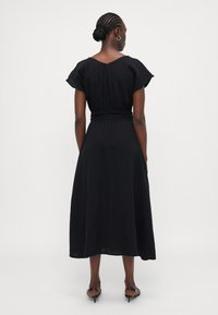 Black, short-sleeve dress with a V-shaped back, cinched waist, and flowing hem. Made from lightweight fabric with a smooth texture.