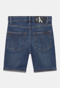 Džínové šortky v tmavě modré barvě s rovný střih, obsahující dvě zadní kapsy s výrazným prošíváním a páskem s logem.