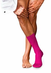 Calcetines de rodilla de color rosa brillante con textura acanalada, usados en un pie, mientras que el otro pie está descalzo y apoyado contra la pierna.