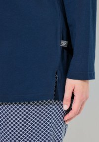 Camiseta de manga larga azul marino con una abertura lateral, hecha de un tejido suave. Combinada con pantalones estampados que presentan un diseño geométrico en blanco y azul.