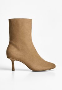 Botă ankle din suede bej, cu vârf ascuțit și toc subțire stiletto. Textură netedă, fără modele sau accesorii vizibile. Siluetă elegantă.