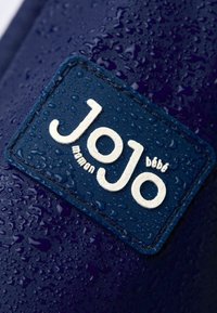 Jūros mėlynos spalvos atsparus vandeniui audinys su lašeliais, su kremine spalva iškilmingu logotipu, kuris skaito "JoJo maman bébè" ant stačiakampio ženklo.