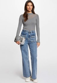 Graues geripptes Langarmoberteil mit transparenten gestreiften Details, kombiniert mit hochtaillierten blauen Jeans im weiten Schnitt und einer silberfarbenen, gesteppten Clutch.
