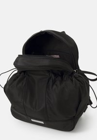 Mochila negra de nylon con un diseño recogido, cordones ajustables, cierre superior con cremallera y una sutil etiqueta plateada en la parte frontal.