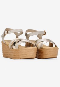 Sandales à plateforme en biseau avec une semelle beige texturée, des brides en métal argenté et une fermeture à boucle. Présente un design croisé et des finitions lisses.