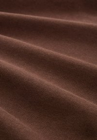 Brauner Strickstoff mit glatter Textur, der subtile Rillen und einen warmen Farbton aufweist. Der Stoff fällt in sanften, fließenden Falten.