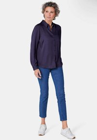 Navy button-up shirt with a collar, long sleeves, and a smooth fabric. Paired with slim blue jeans and white sneakers.