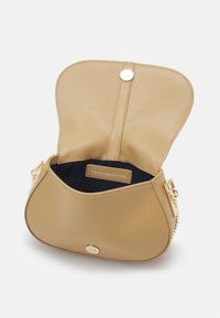 Borsa in ecopelle beige a forma arrotondata, con hardware dorato, chiusura magnetica e interno blu con etichetta del marchio.
