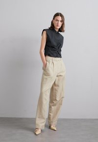 Cămașă neagră fără mâneci cu un nod în față, asortată cu pantaloni largi de un bej deschis și balerini bej. Design minimalist și textură.