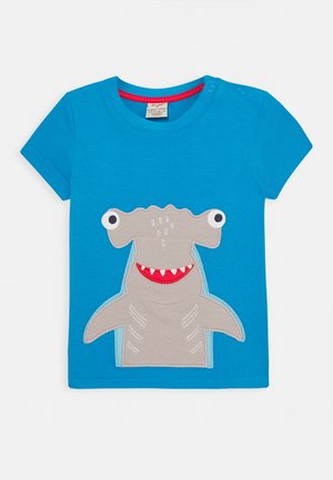 Jasnoniebieska koszulka dla malucha z dużym, szarym rekinem młotem, który ma wystające oczy na szypułkach oraz czerwony, uśmiechnięty pysk z białymi zębami.