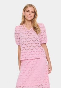 Top in pizzo rosa con maniche a sbuffo corte, scollatura a V e motivo scallop. Abbinato a una gonna coordinata, creando un look armonioso.