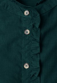 Tissu en velours côtelé vert foncé avec trois boutons ronds clairs et un bord froncé le long de la couture des boutons.