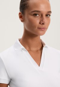 Biała koszulka polo z dekoltem w serek i krótkimi rękawami, o miękkiej fakturze i z pojedynczym guzikiem przy kołnierzyku.