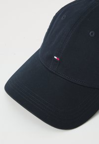 Casquette de baseball bleu marine en coton avec une visière incurvée. Présente un petit logo rouge, blanc et bleu sur le panneau avant et des coutures visibles.