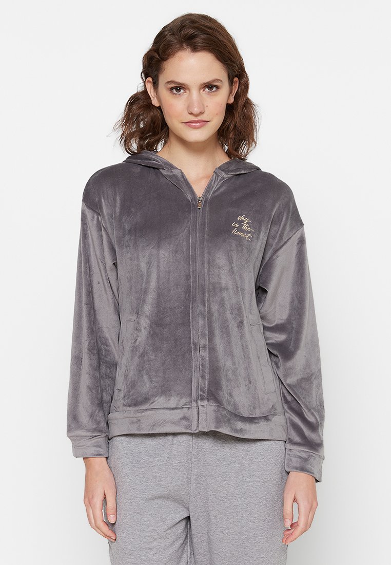 Grijze velours zip-up hoodie met een voorkleur, trekkoordkap en gouden tekstdetail. Zachte textuur en een ontspannen pasvorm.
