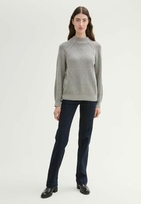 Maglione grigio a costine con un colletto alto, abbinato a jeans dritti blu scuro e stivali neri alla caviglia. Design semplice e strutturato.