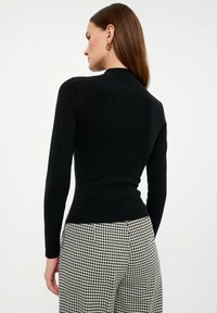 Top in maglia nera a maniche lunghe con collo alto, abbinato a pantaloni a scacchi bianchi e neri. Tessuto liscio e design aderente.