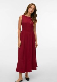 Burgundijas bezpidurņu kleita ar pieguļošu augšu, izplūdušu svārku un šuvju detaļām. Gluda auduma ar matētu apdari. Apvienota ar melnajām kurpēm.