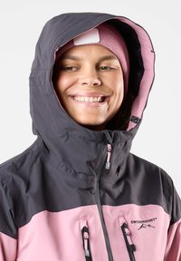 Hoodie mit einem schwarz-pinken Farbschema, strapazierfähigem Stoff, verstellbaren Reißverschlüssen und einem Logo auf der Brust. Glatte Innenstruktur.