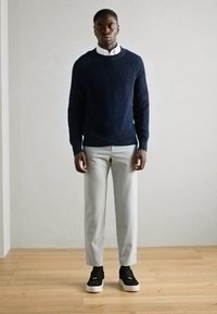 Marineblå strikkegenser, lysegrå bukser og svarte joggesko. En enkel design med ribbestruktur, plassert mot en nøytral bakgrunn.
