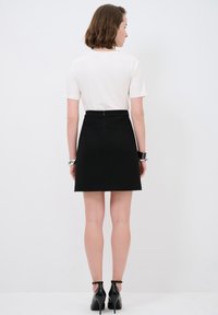 Zwarte kokerrok met een hoge taille en een ritsdetail aan de achterkant, gecombineerd met een plain witte T-shirt met korte mouwen en zwarte hakken.