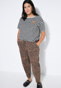 Camiseta a rayas en blanco y negro con un parche en forma de corazón con estampado de leopardo, combinada con pantalones de chándal marrones con estampado de leopardo. Zapatos negros sencillos.