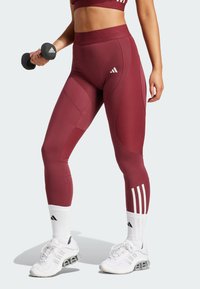 Bordeaux atletiske leggings med ribbet tekstur, der har en høj talje og accentpaneler. Båret sammen med hvide sokker og sko, mens der holdes en håndvægt.