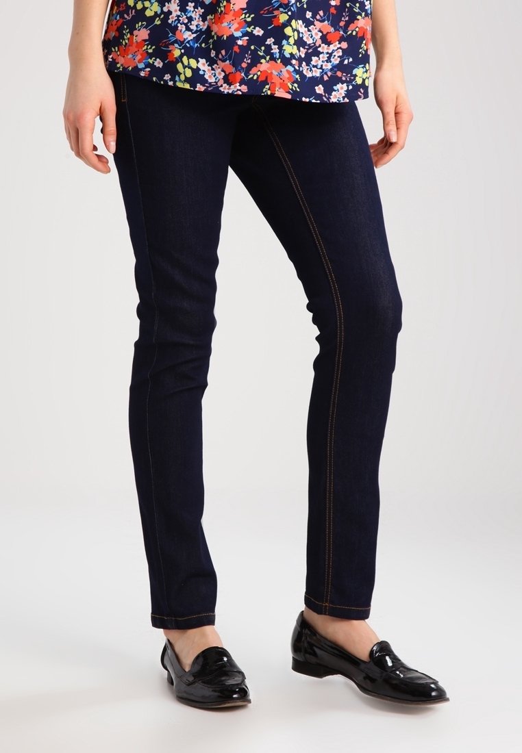 Tmavě modré skinny džíny s kontrastním oranžovým šitím, vyrobené z denimu, v kombinaci s černými lakovanými mokasíny.