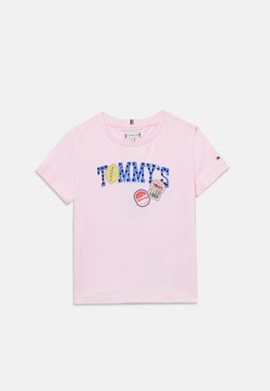 Hellrosa kurzärmeliges T-Shirt mit "TOMMY'S" in blauen Buchstaben und bunten, kreisförmigen Grafikaufnähern auf der Vorderseite.