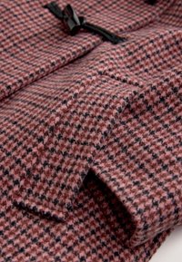 Manteau en tissu de laine à motif à carreaux rose et noir, présentant une texture lisse et une fermeture à brandebourg noire. Vue en gros plan du matériau plié.