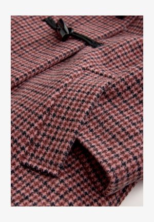 Cappotto in tessuto di lana con motivo a quadri rosa e nero, caratterizzato da una texture liscia e chiusura con bottoni a gancio neri. Vista ravvicinata del materiale piegato.