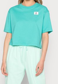 Camiseta corta de color turquesa hecha de algodón, con un logo de Jordan en un parche blanco y mangas cortas. Combinada con pantalones de chándal en un tono verde menta claro.