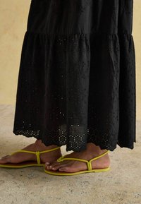 Czarna, haftowana sukienka maxi z warstwowym krojem. W zestawie z żółtymi płaskimi sandałami o minimalistycznym wzorze pasków.