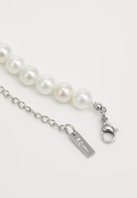 Pearl bracelet with alternating white and cream pearls, featuring a silver chain and lobster clasp, with a rectangular tag detail.
