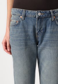 Blugi din denim de culoare albastru deschis, cu un design cu picior drept, cu nituri din cupru și închidere buton. Prezintă decolorări subtile și detalii clasice de coasere.