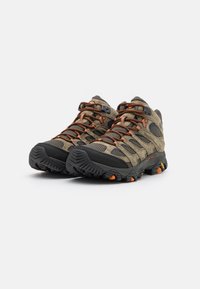 Buty trekkingowe w oliwkowym zielonym i czarnym kolorze, z materiałami z siateczki i zamszu, z pomarańczowymi akcentami oraz wytrzymałą podeszwą z wzorami zapewniającymi przyczepność.