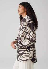 Camicia a maniche lunghe con un motivo astratto di foglie in bianco e nero, realizzata in un tessuto leggero con una vestibilità comoda e colletto con bottoni.