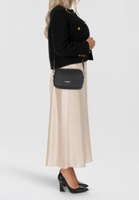 Borsa a tracolla nera in pelle con hardware argentato, texture liscia, forma rettangolare, caratterizzata da un logo e tracolla regolabile.